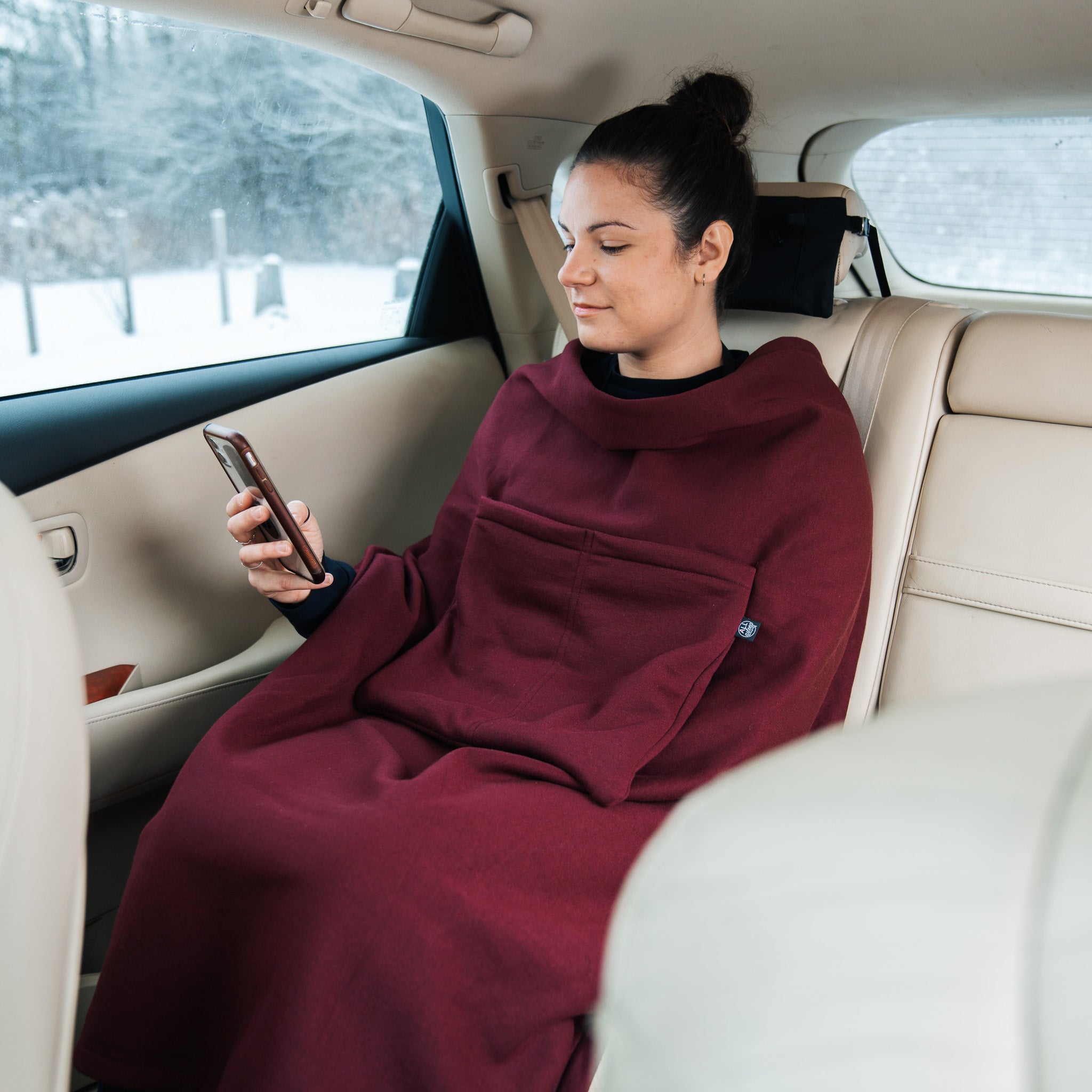 Woman sitting in a car looking at her phone with her travel blanket on