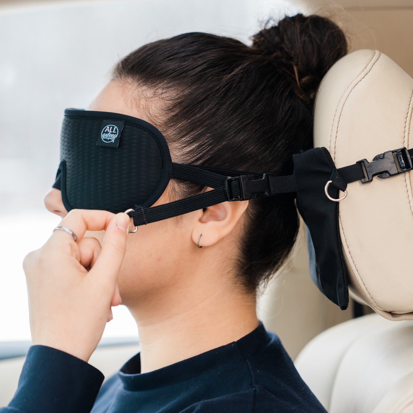 Woman sitting in the car adjusting the mask straps of the ALLasleep travel accessory