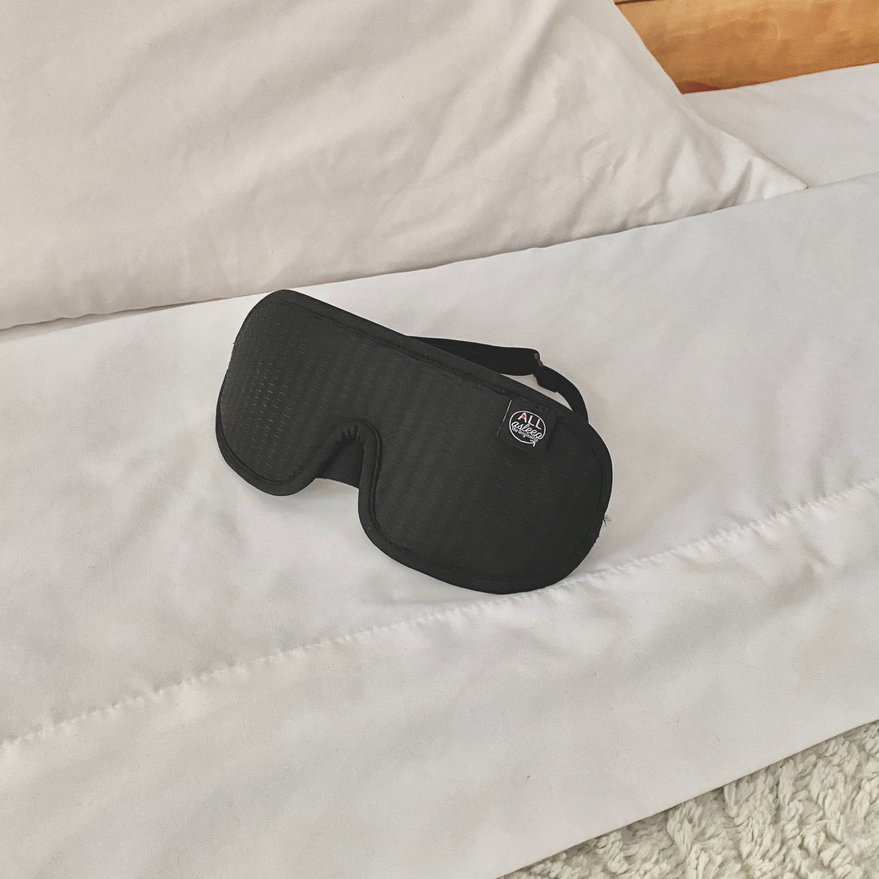 ALLasleep sleep mask laying near the pillow of a bed